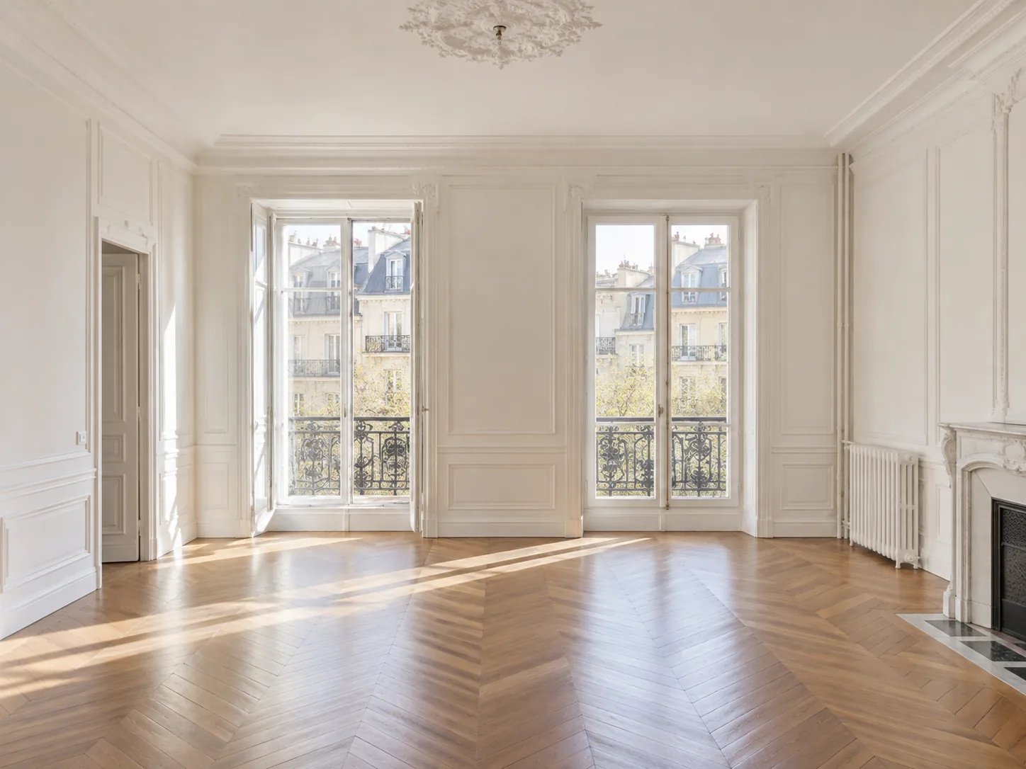 Un séjour parisien vide, parquet en point de Hongrie et deux hautes fenêtres